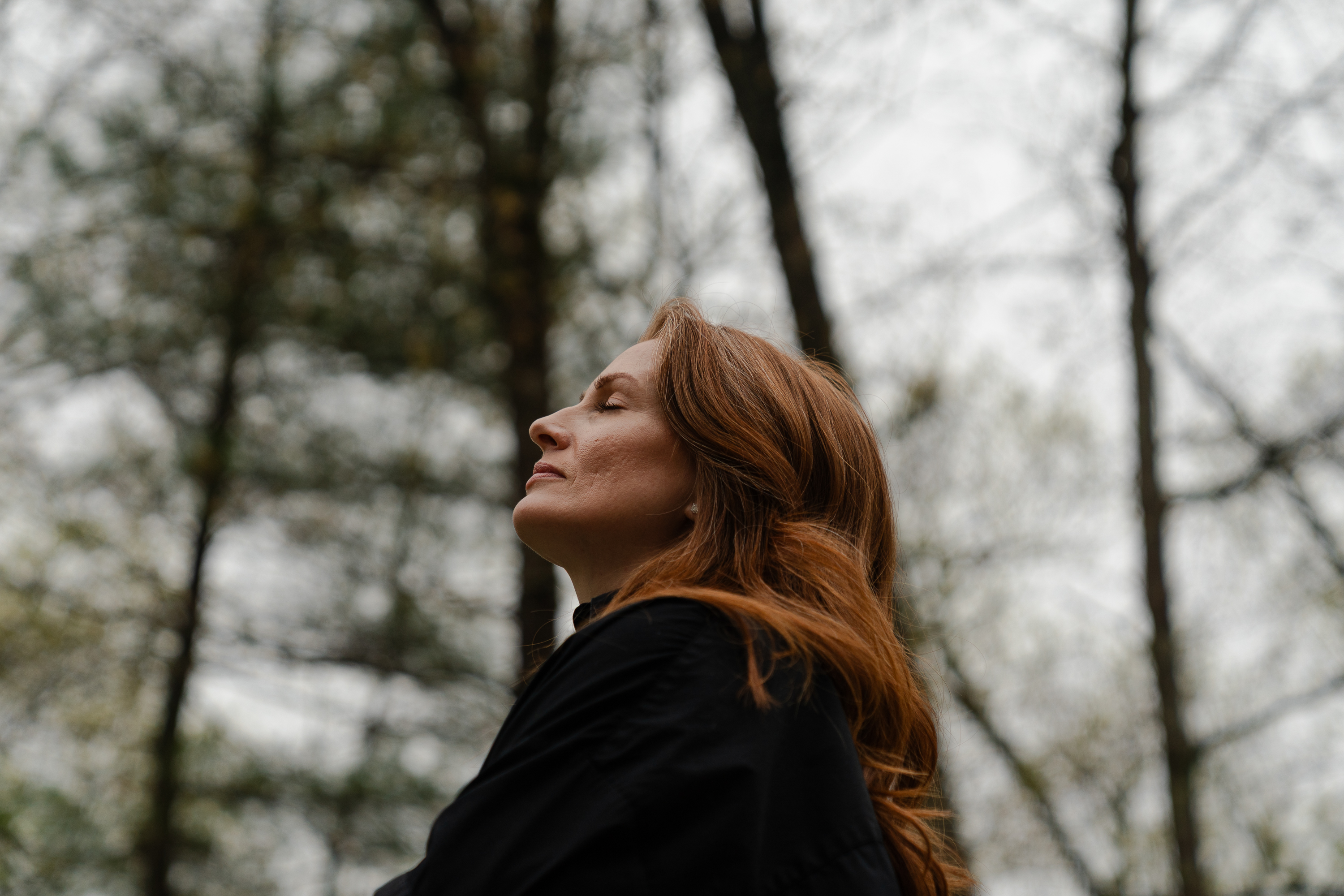 Red-haired woman outside with her eyes closed, seen from a low angle.
