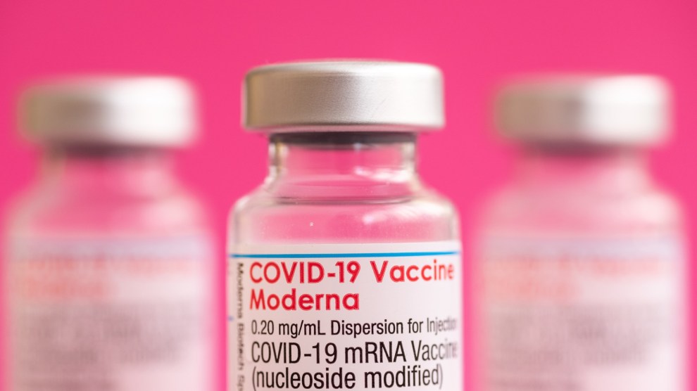 Three vials of Covid vaccine in front of a bright pink background