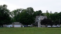 A two-story house surrounded by trees, with several law enforcement vehicles parked outside.