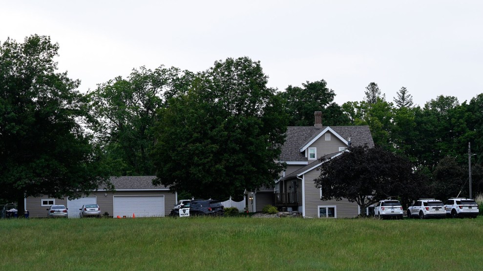A two-story house surrounded by trees, with several law enforcement vehicles parked outside.