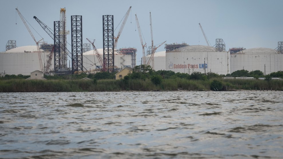 Large white liquid natural gas tanks surrounded by cranes are seen from across a river