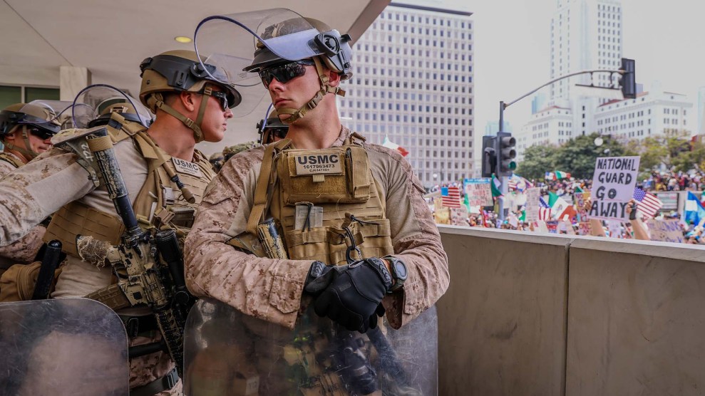A Marine man in uniform looks away from the protestors in a city. Another looks towards them.