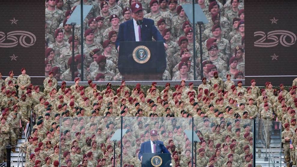 Donald Trump on stage in front of a crowd of soldiers, with a big screen showing him in the background