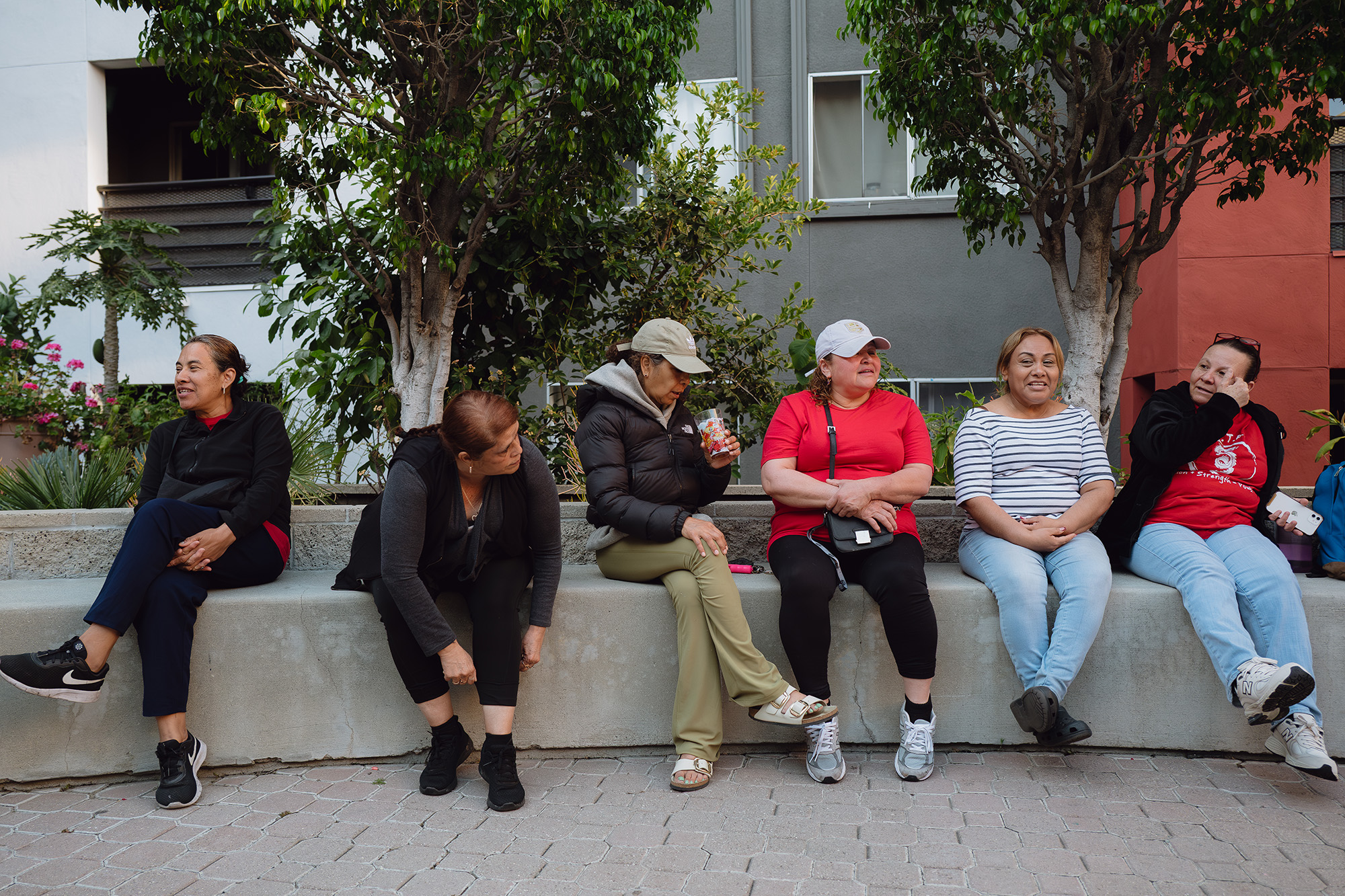 Six women sit on a concrete bench in the courtyard of Hillside Villa, an affordable housing complex in Los Angeles.