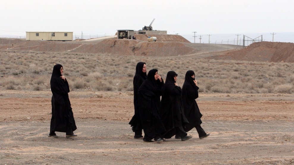 Five women walk across the dry earth with machinery in the background.