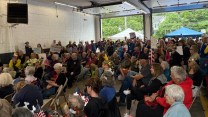 A crowd of people sitting in foldable chairs, inside a garage.