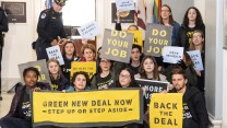 A group of youth hold yellow and black signs that say "Green New Deal Now"