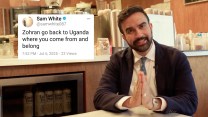 Zohran Mamdani is wearing a suit and tie, and sitting at a table with his hands clasped in front of him, appearing to speak or gesture toward the camera. On the left side of the image is a screenshot of a tweet from user @samwhite087 that reads: “Zohran go back to Uganda where you come from and belong.”