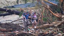 Image of a couple carrying children and climbing over debris on a bridge atop the Guadalupe River.
