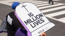 Someone holding up a sign outside that shaped like a grave that says "16 million lives" on it.