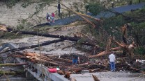 Logs and branches cover a bridge and tower of a couple people sifting through them.