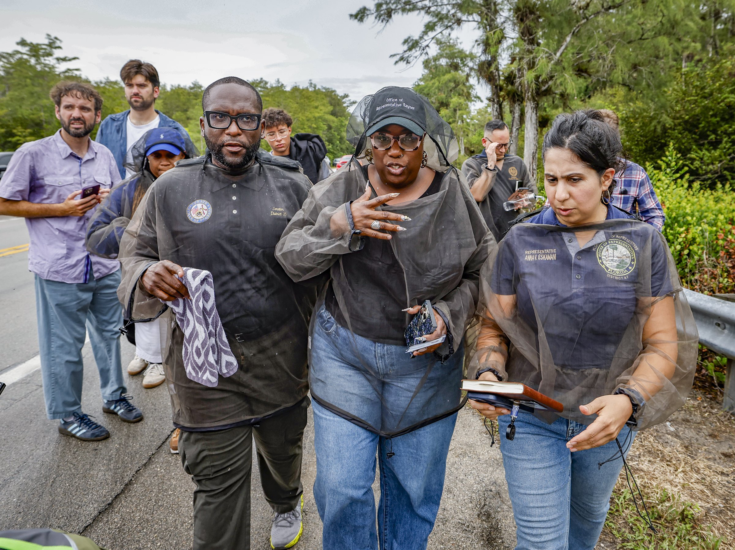 Sen. Shevrin Jones, State Rep. Michele K. Rayner and Rep. Anna V. Eskamani, PhD walk together outside of a detention center in Florida; they don mosquito netting and boots.