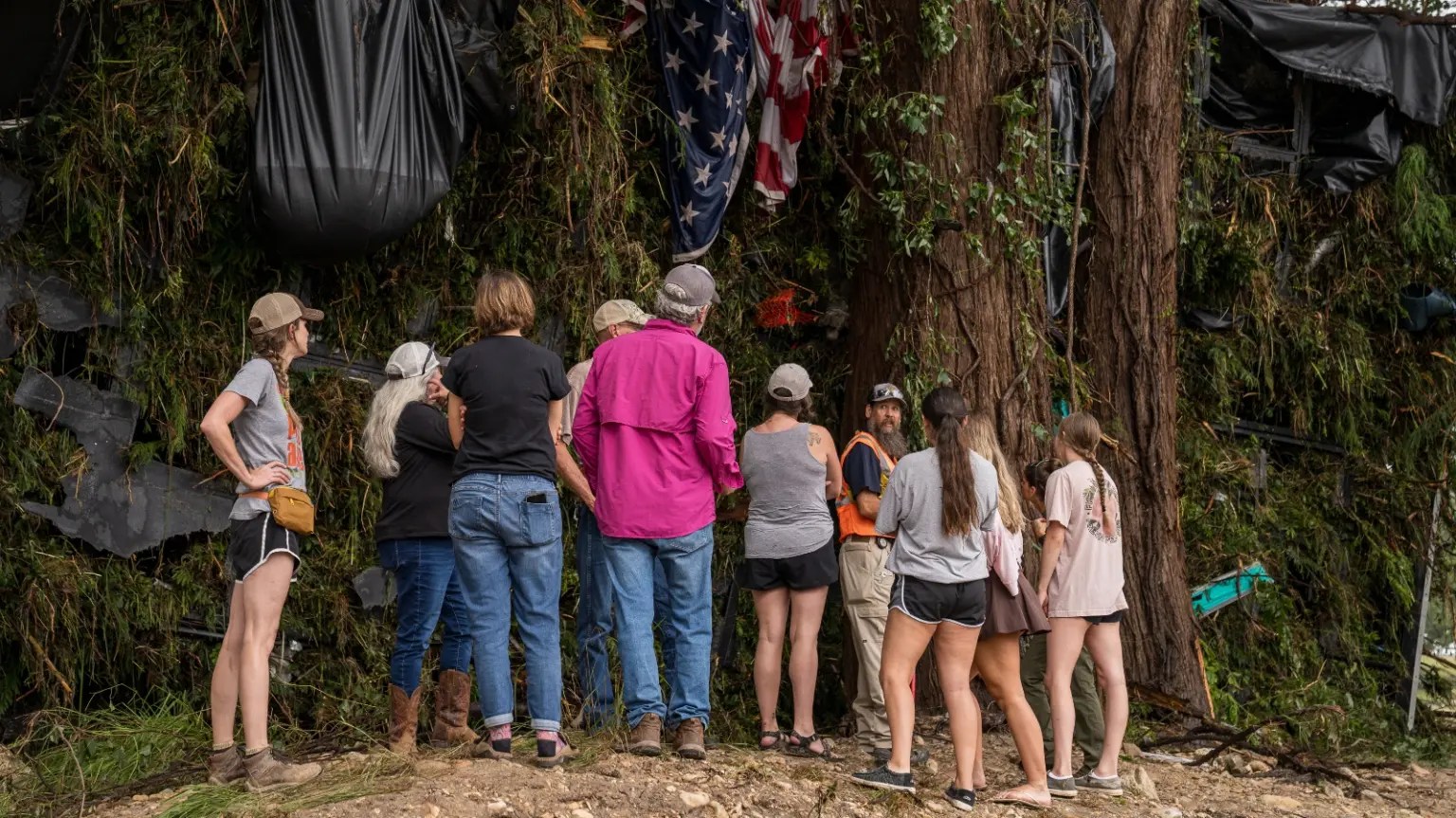 Six figures look at debris, including an American flag, caught up in trees and branches.