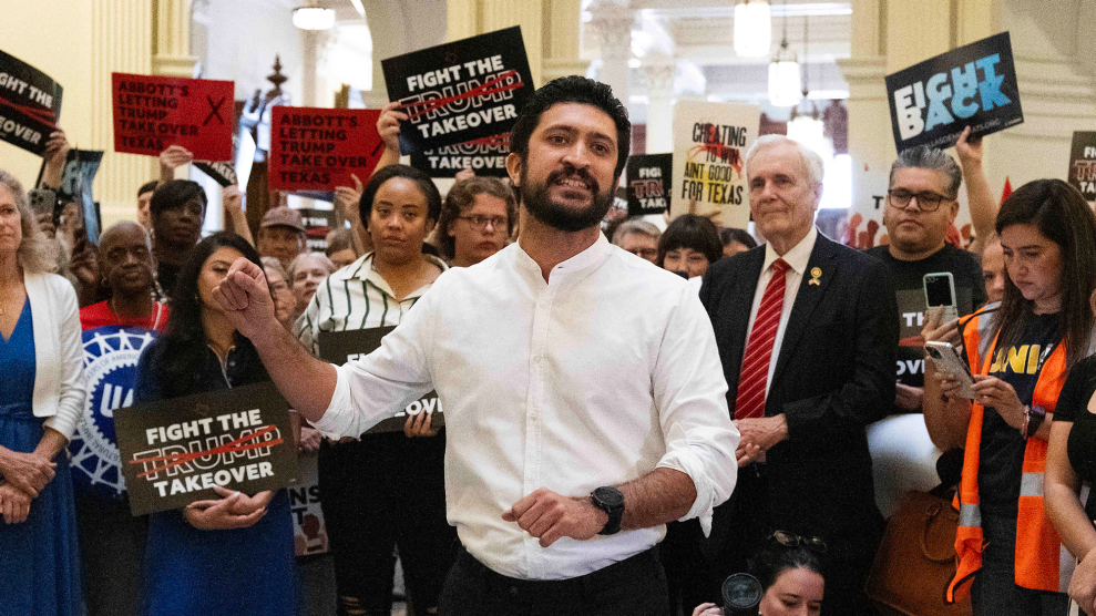 A young man with dark hair and a beard, wearing a white shirt with rolled up sleeves, speaks passionately in front of dozens of people. Some of the people hold signs, which read "Abbott's letting Trump take over Texas," "Fight the Trump takeover," and "Fight back."