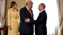 Donald Trump shakes hands warmly with Vladimir Putin as Melania Trump looks on.
