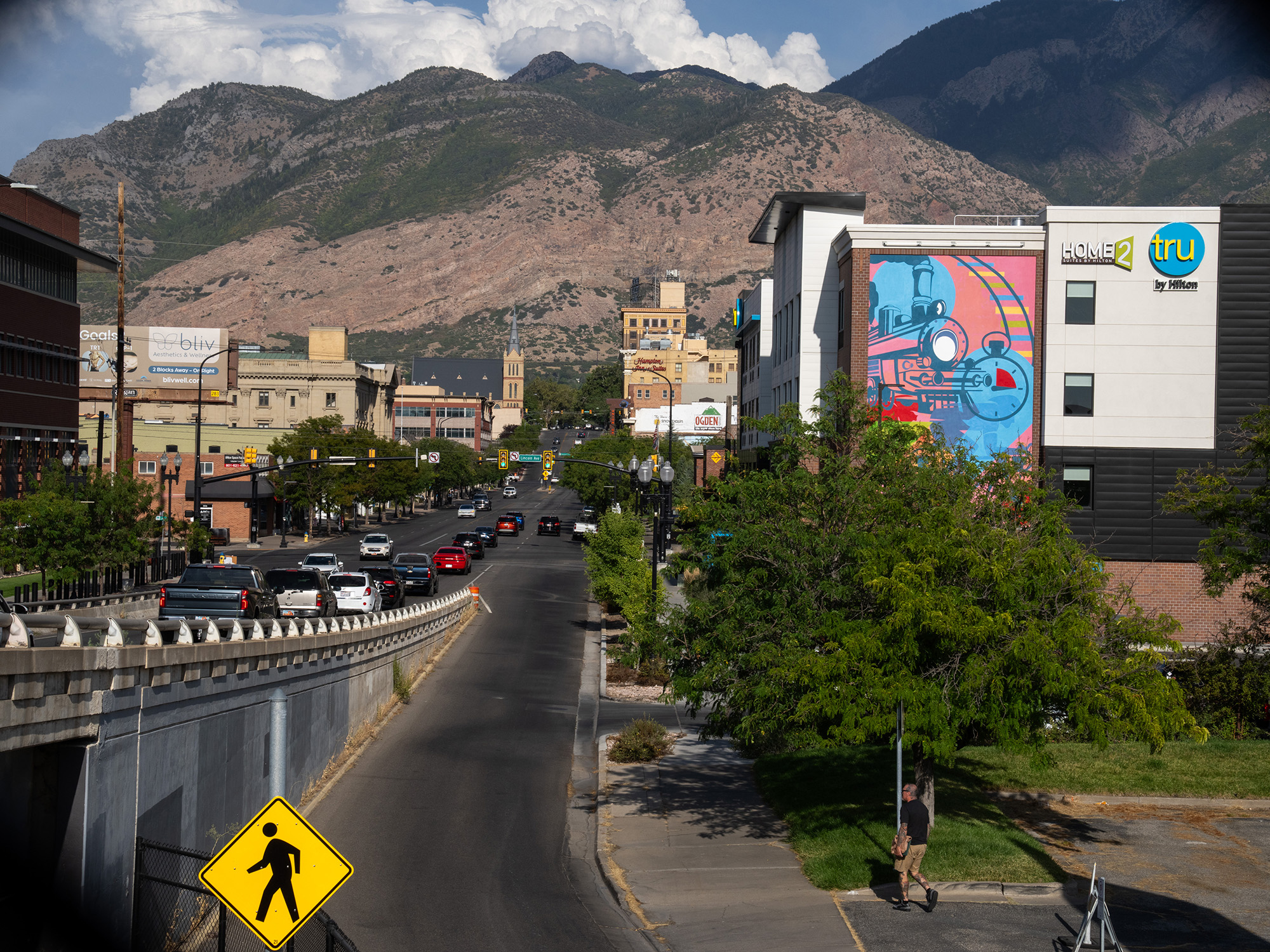 View of a street in Ogden with mountains in the distance on a sunny day. One building features a brightly painted mural.