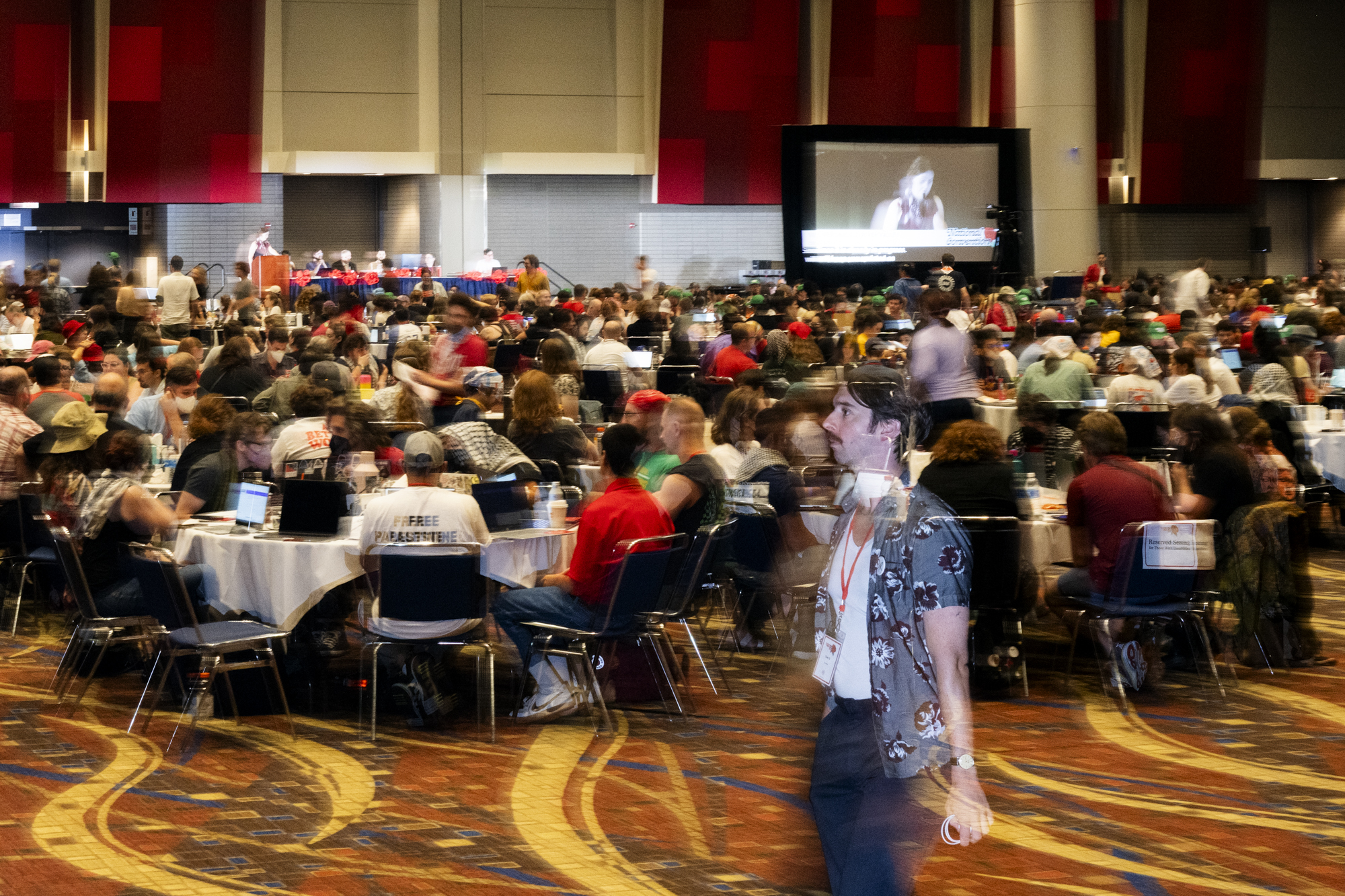 Man walking past cluster of tables in convention center room.