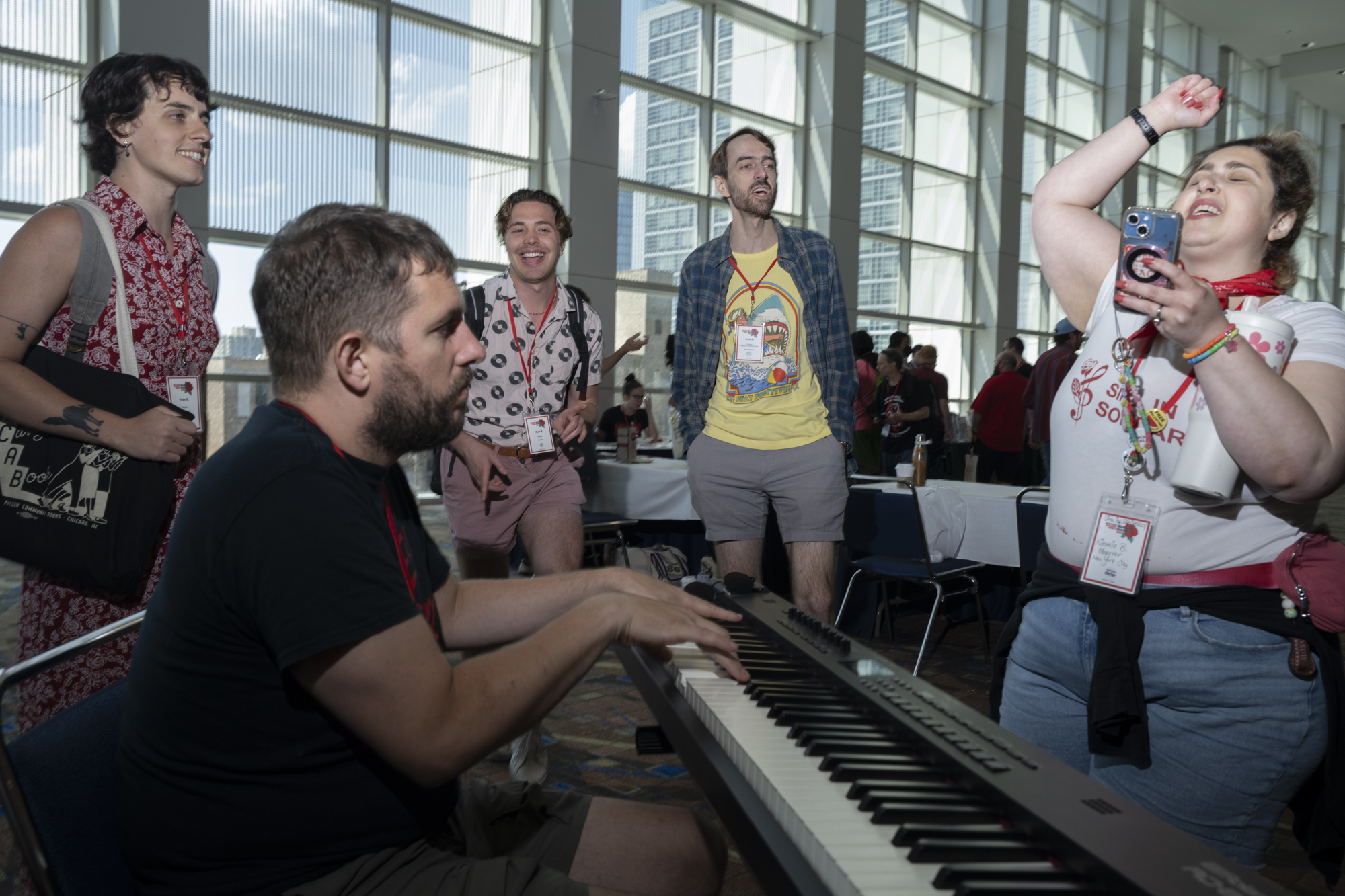 Group of people singing around a man playing a piano.