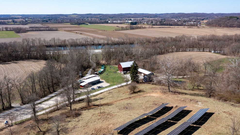 Solar panels on a field next to a barn and a small clump of trees.