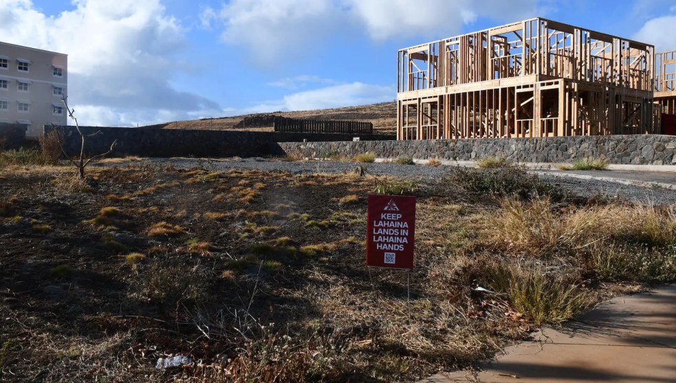 An empty lot with a wood-frame house with the sign "keep Lahaina lands in Lahaina hands"