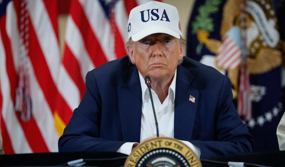 Donald Trump sits at a table behind a presidential seal. Beads of sweat are visible on his face.