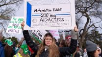 A woman holding up a hand-drawn sign depicting a box of mifepristone tablets at an outdoor protest for abortion rights in Washington, DC.