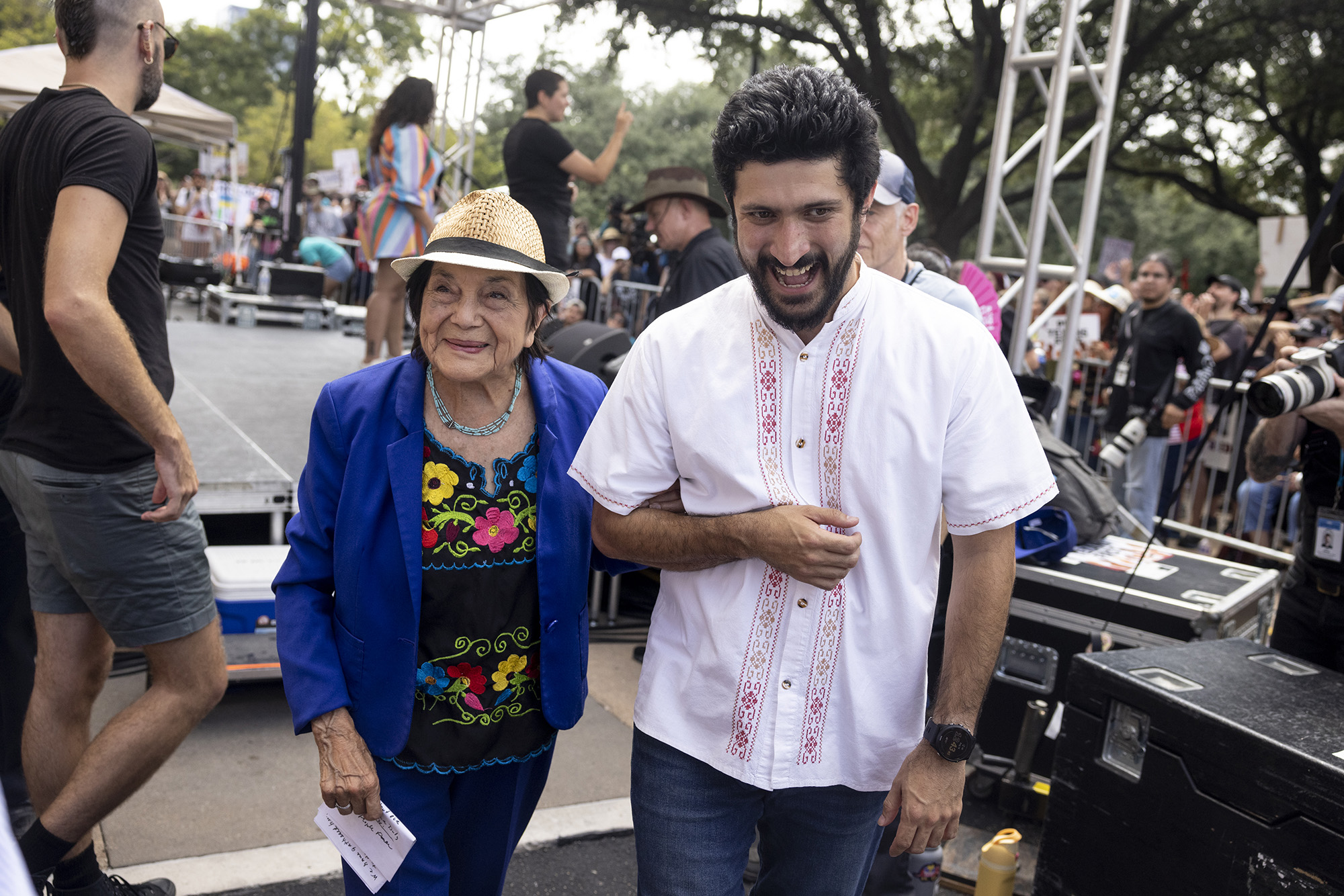 Greg Casar walks away from an outdoor stage arm in arm with Dolores Huerta.