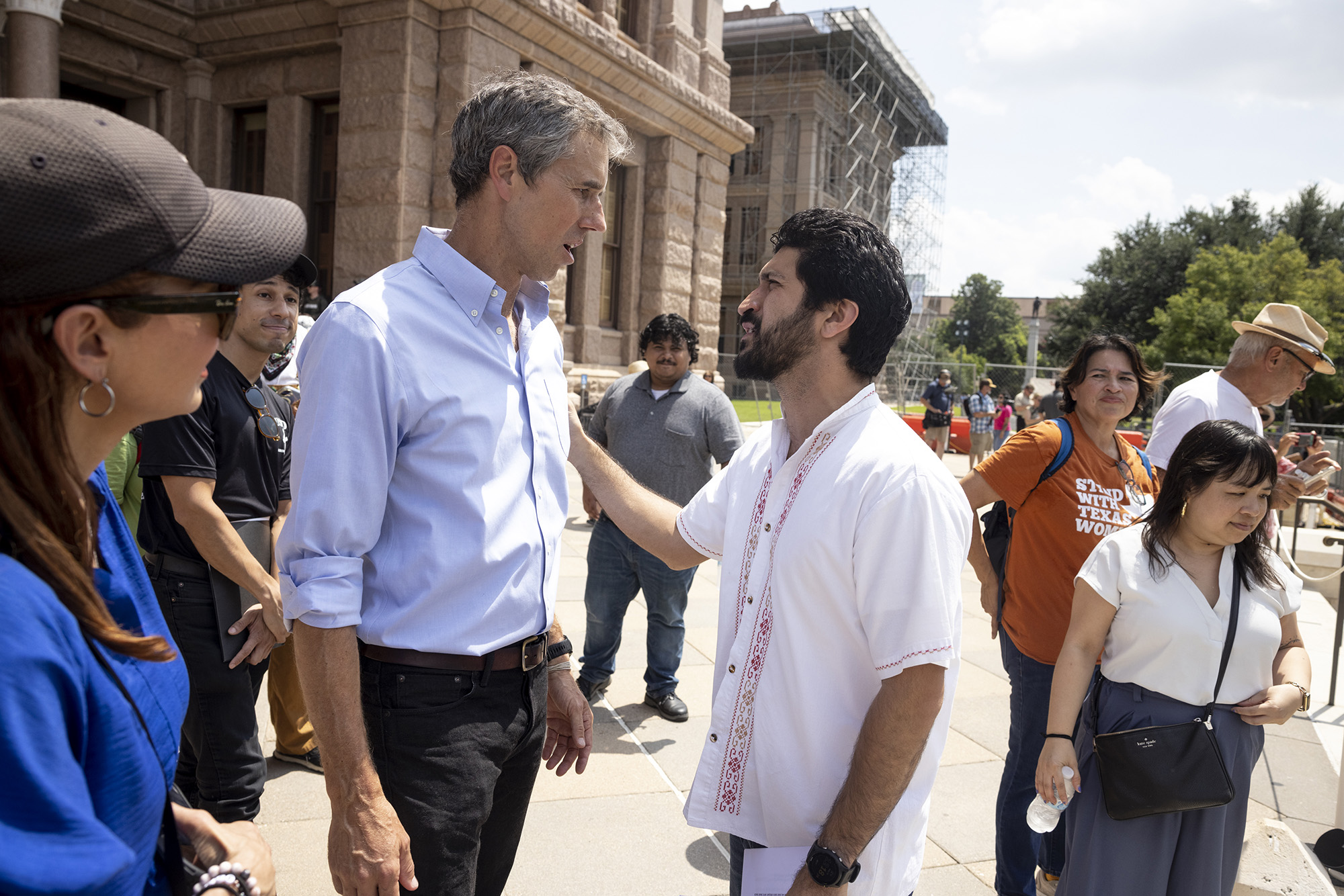 Greg Casar and Beto O'Rourke face each other while speaking. Casar's right hand rests on O'Rourke's left shoulder.