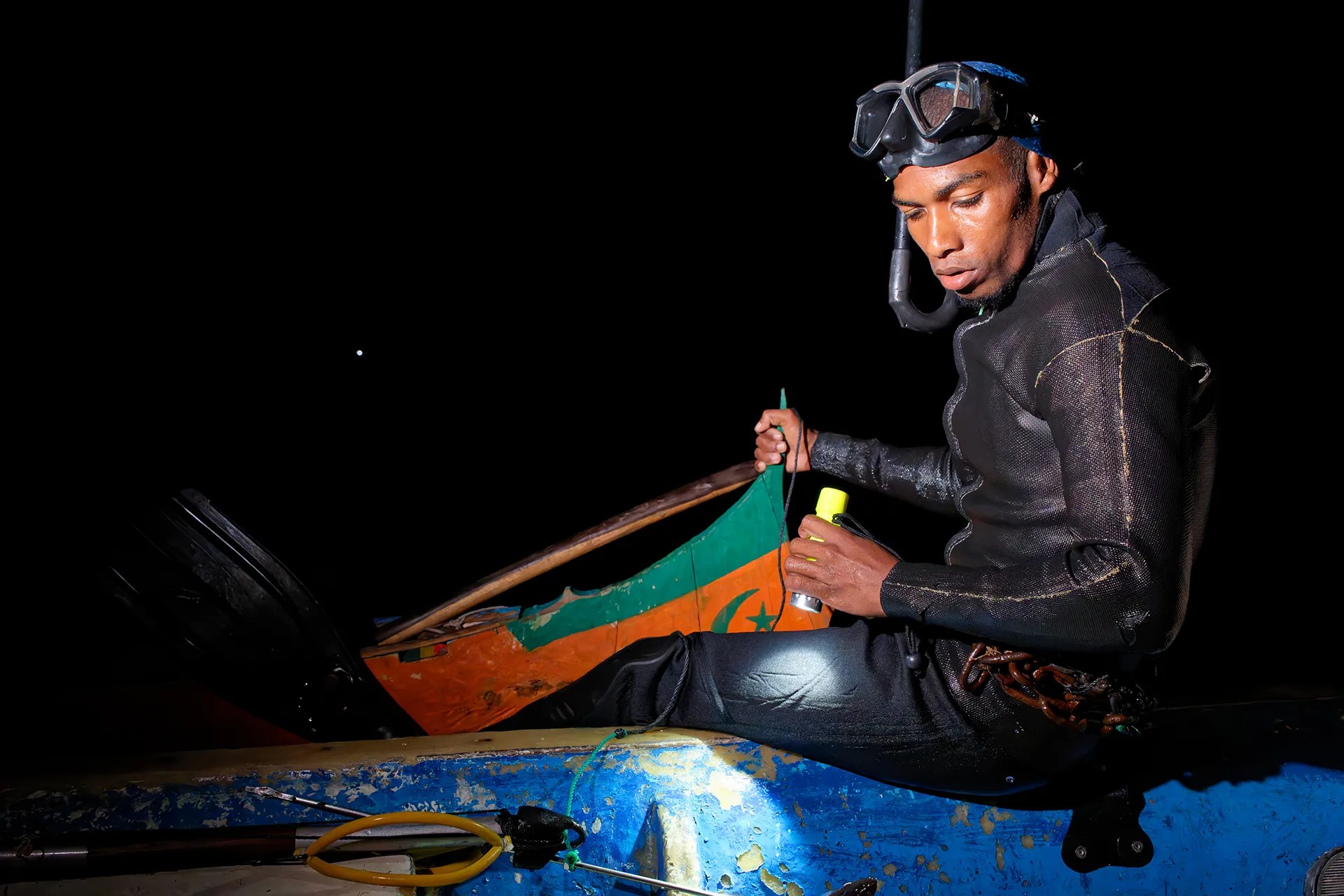 A man wearing a wetsuit shines a light on a boat.