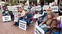 A group of people sitting and standing holding signs to raise awareness for black lung.
