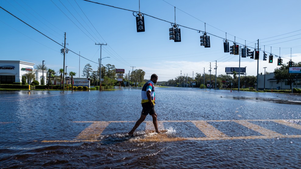 A person walks on a cross walk that is ankle deep flooded in water.