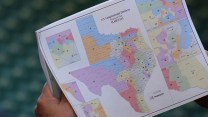 A hand holds a sheaf of papers topped by a proposed Texas congressional map.