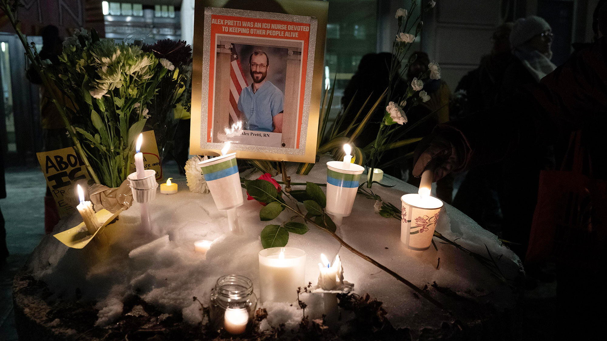 Memorial for Alex Pretti with a photo of him in scrubs surrounded by candles and flowers.