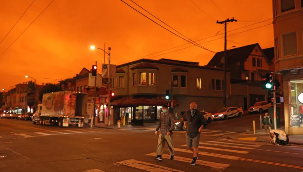 Two people walk across a street wearing masks in a city with an orange sky.