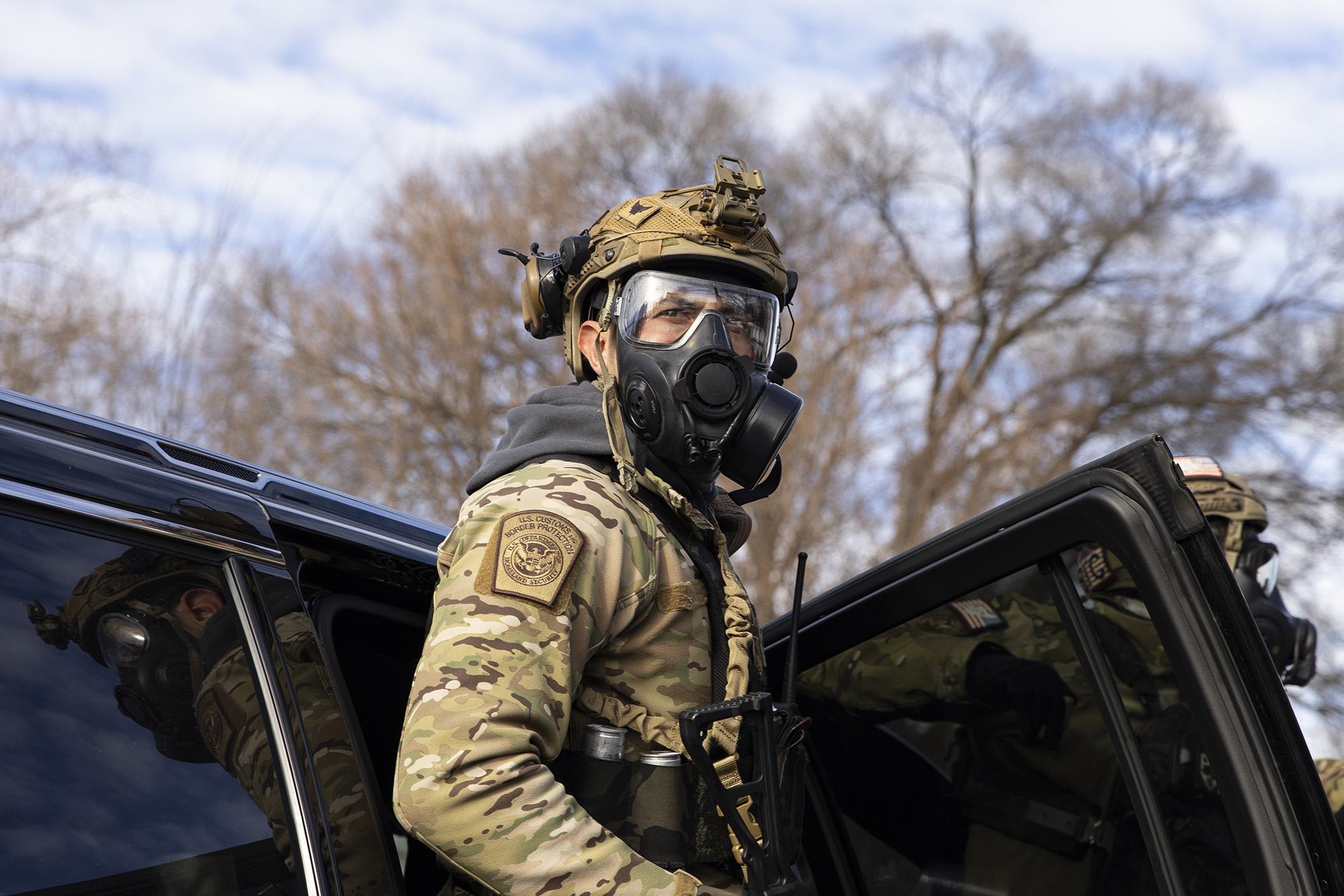 A federal agent in a gas mask exits an SUV.