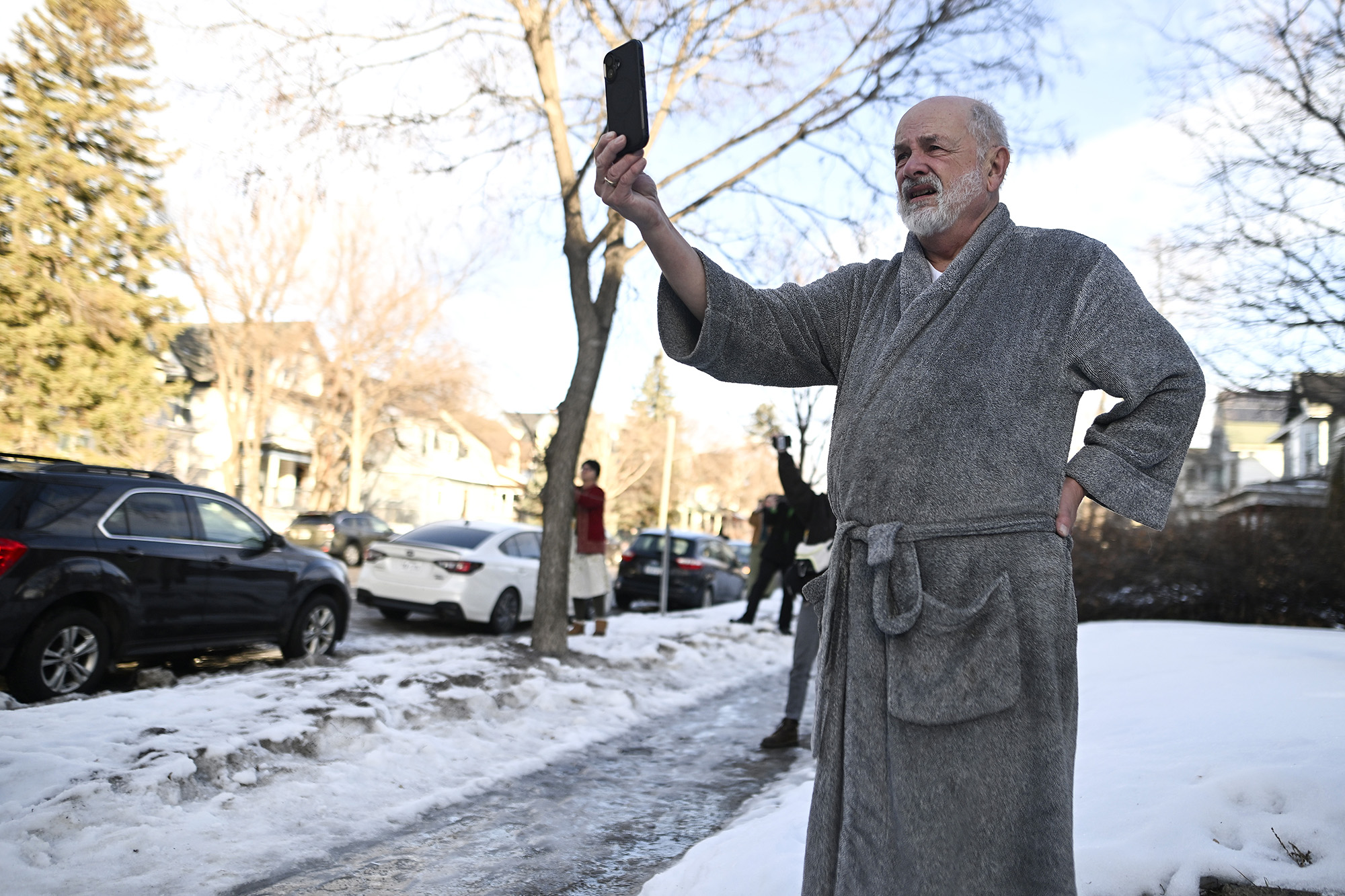 A man in a bathrobe standing in the snow films ICE agents.